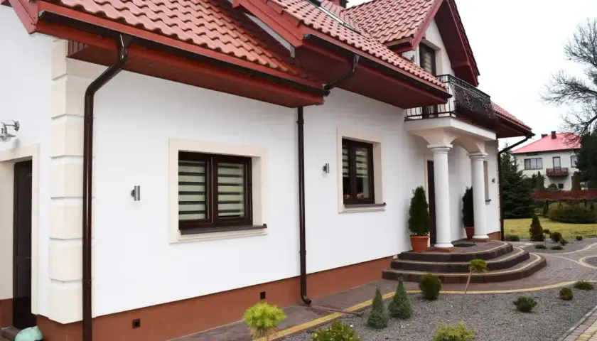 Nowy, biały tynk elewacji lśni na słońcu, podkreślając nowoczesny styl domu.