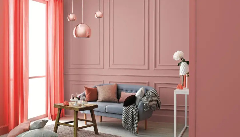 Przytulny salon w odcieniach różu i koralu. Na ścianach subtelny wzór, a w centralnym punkcie wygodna kanapa. Kolor waniliowy subtelnie podkreśla elegancję wnętrza.