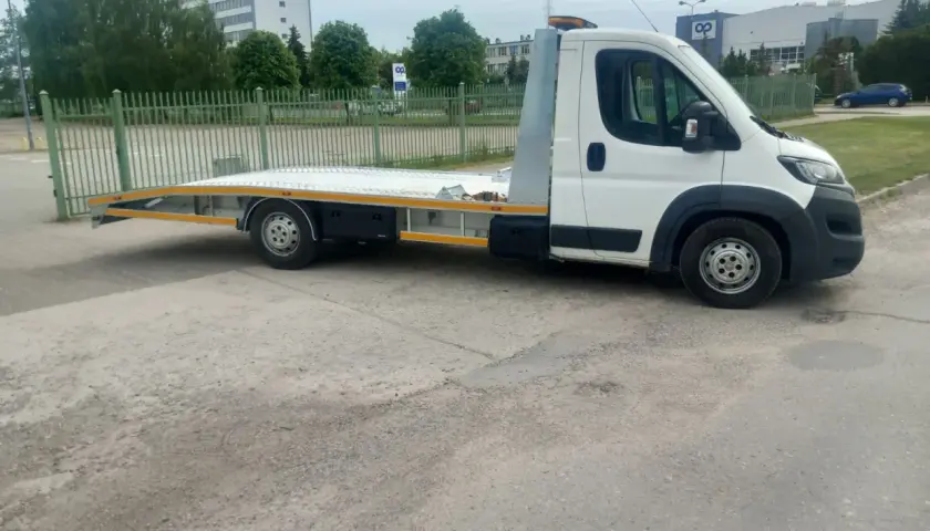 Biała laweta z platformą stoi na parkingu. Zastanawiasz się, ile kosztuje laweta?