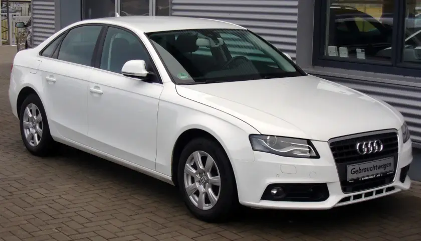 Białe Audi A4 B8 sedan zaparkowane na bruku przed budynkiem.