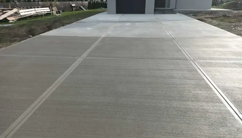 Nowy podjazd z beton stemplowany, z wyraźnymi liniami podziału, prowadzi do nowoczesnego domu.