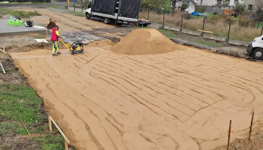 Pracownik zagęszcza piasek zagęszczarką. Trwają prace ziemne, ustalana jest korytowanie cena za m2.