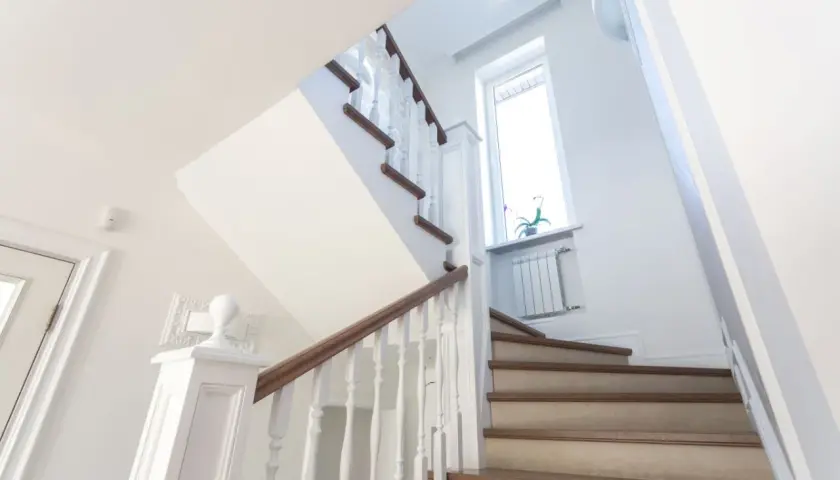 Jasne schody z drewnianymi stopniami i białymi balustradami. Inspiracja, jak tanio wykończyć schody betonowe, by wyglądały elegancko.