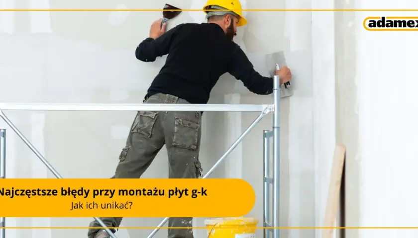 Fachowiec w żółtym kasku i roboczych spodniach pracuje na rusztowaniu, nakładając gładź na ścianę. To praca przy **suchej zabudowie**.