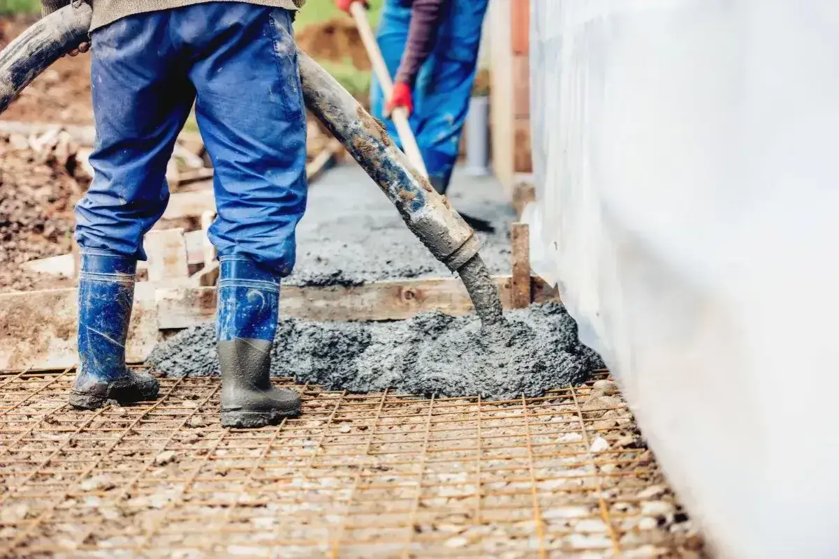 Pracownicy wylewają beton na zbrojenie. Sprawdź aktualną suchy beton cena 1m3.