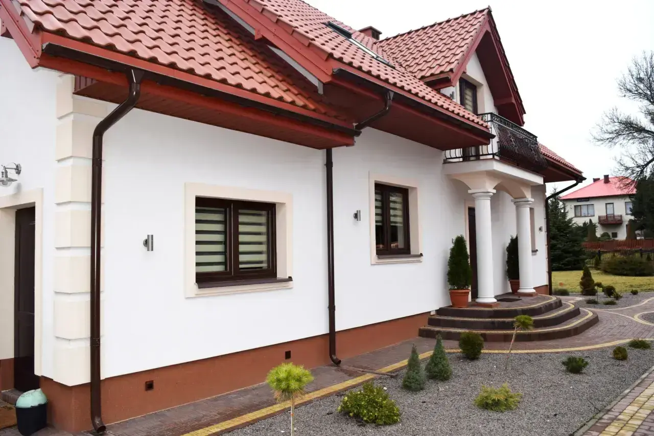 Nowy, biały tynk elewacji lśni na słońcu, podkreślając nowoczesny styl domu.