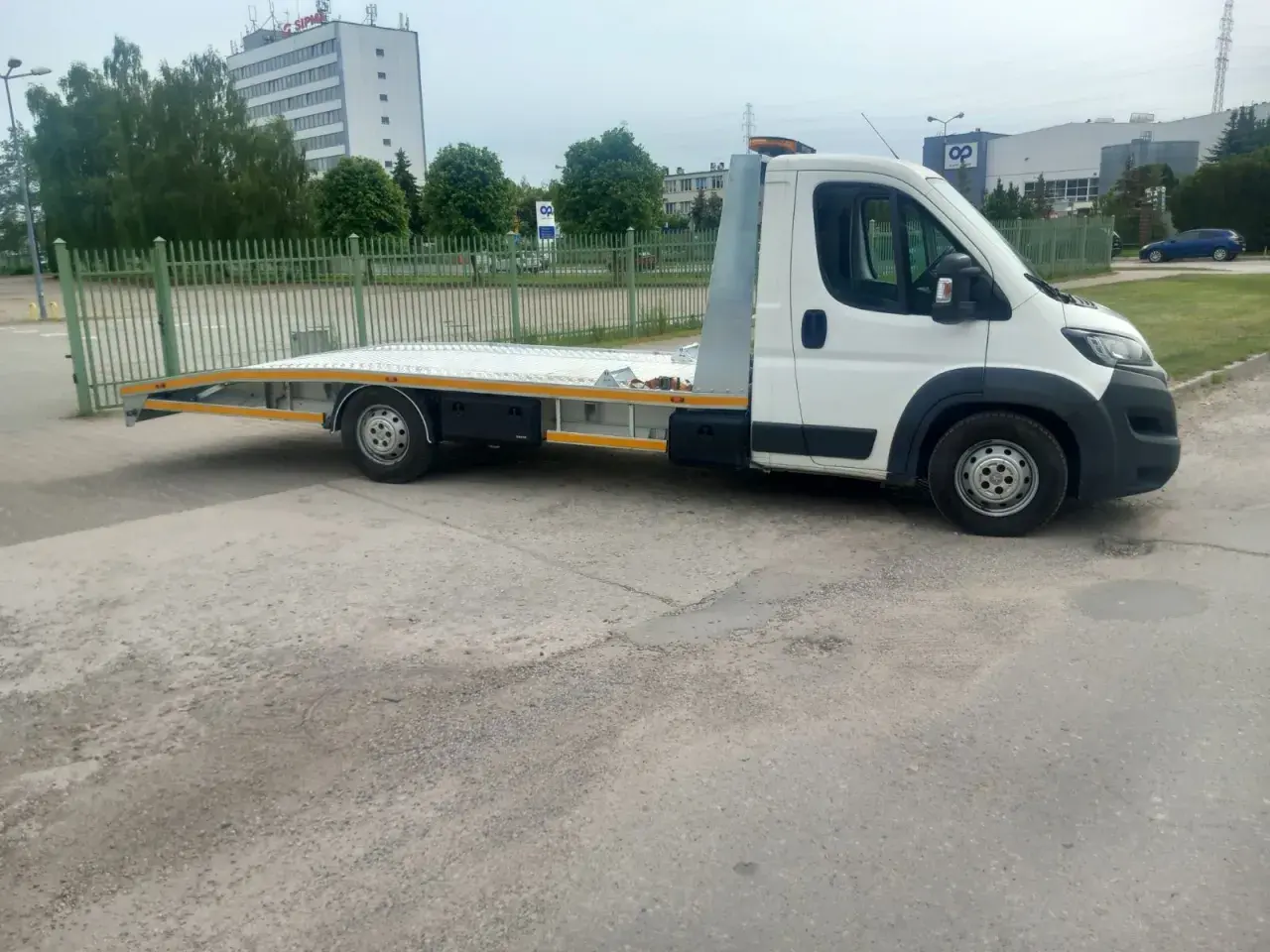Biała laweta z platformą stoi na parkingu. Zastanawiasz się, ile kosztuje laweta?