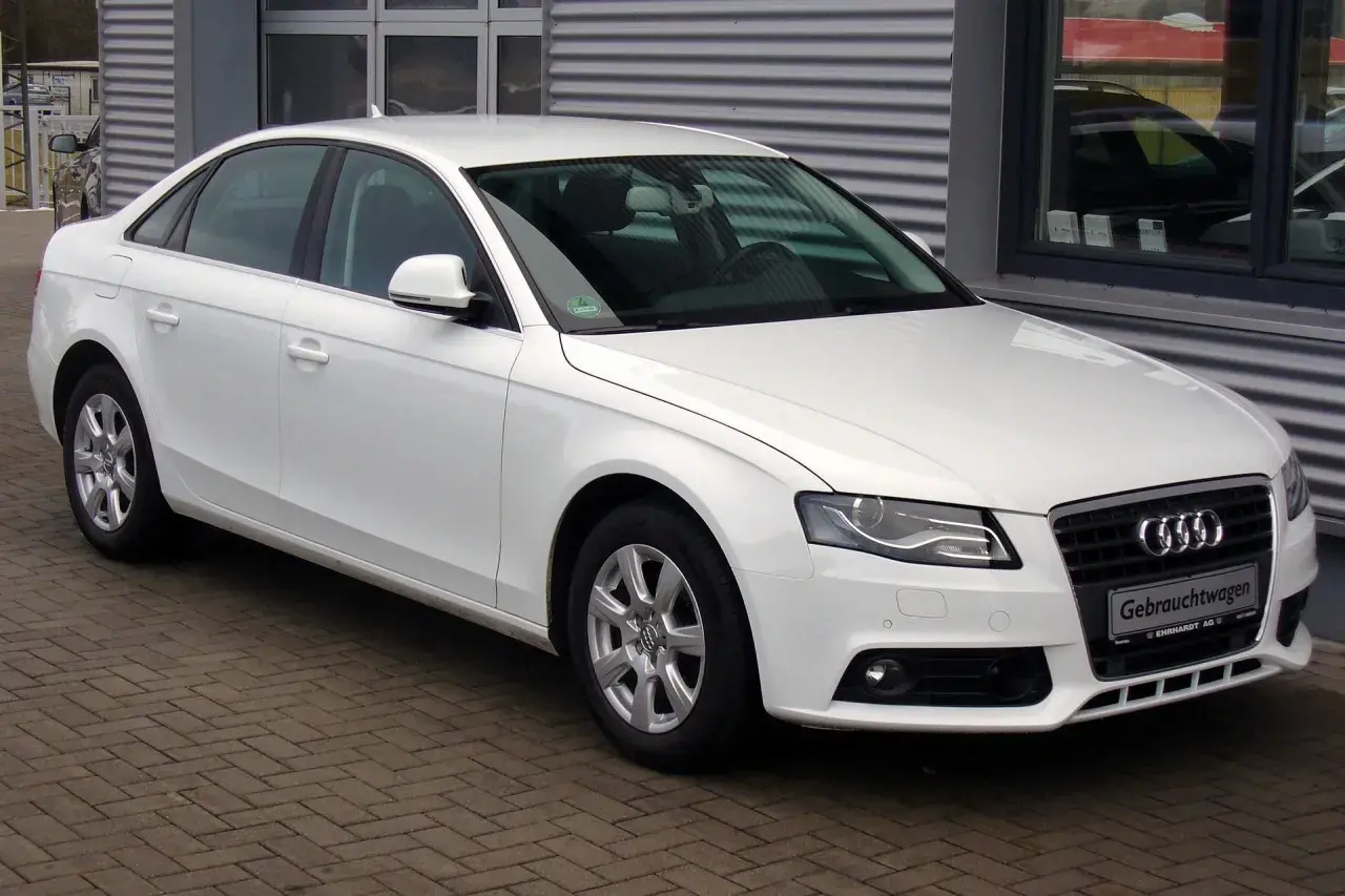 Białe Audi A4 B8 sedan zaparkowane na bruku przed budynkiem.