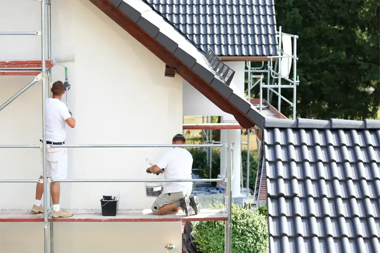 Dwóch mężczyzn na rusztowaniu maluje białą elewację. Sprawdzają tynk silikonowy cena za m2 robocizny.