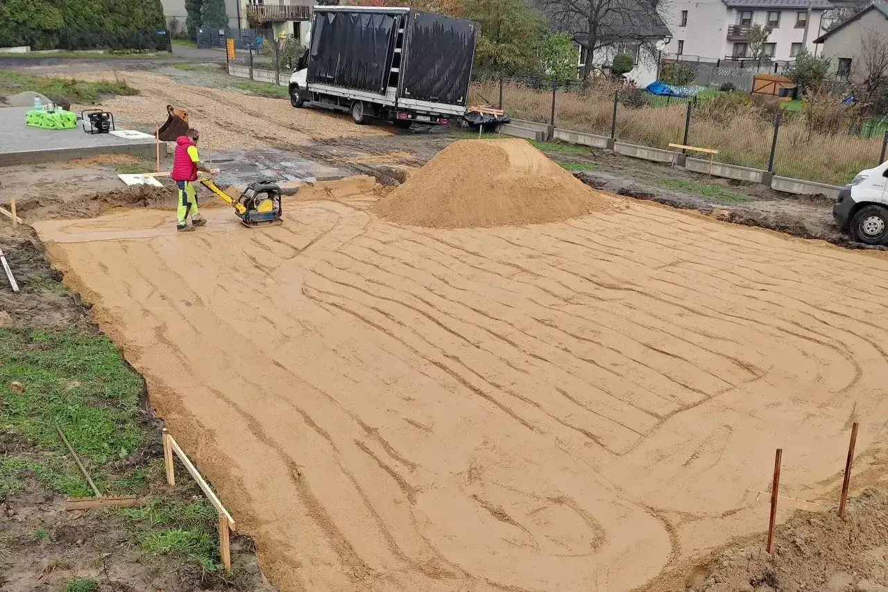 Pracownik zagęszcza piasek zagęszczarką. Trwają prace ziemne, ustalana jest korytowanie cena za m2.