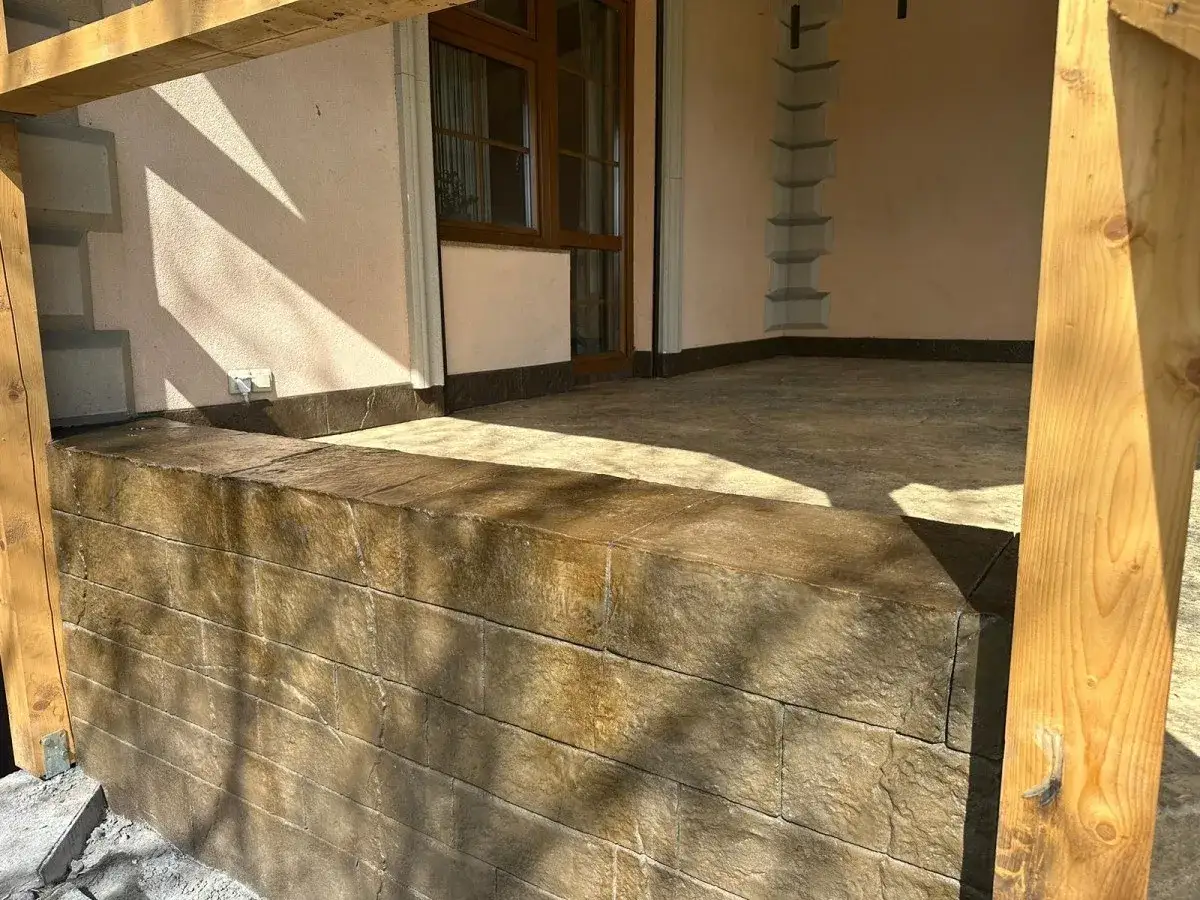 Nowoczesny taras z efektem kamienia. Beton stemplowany imituje cegłę na murku i płytki na posadzce, tworząc spójną całość.
