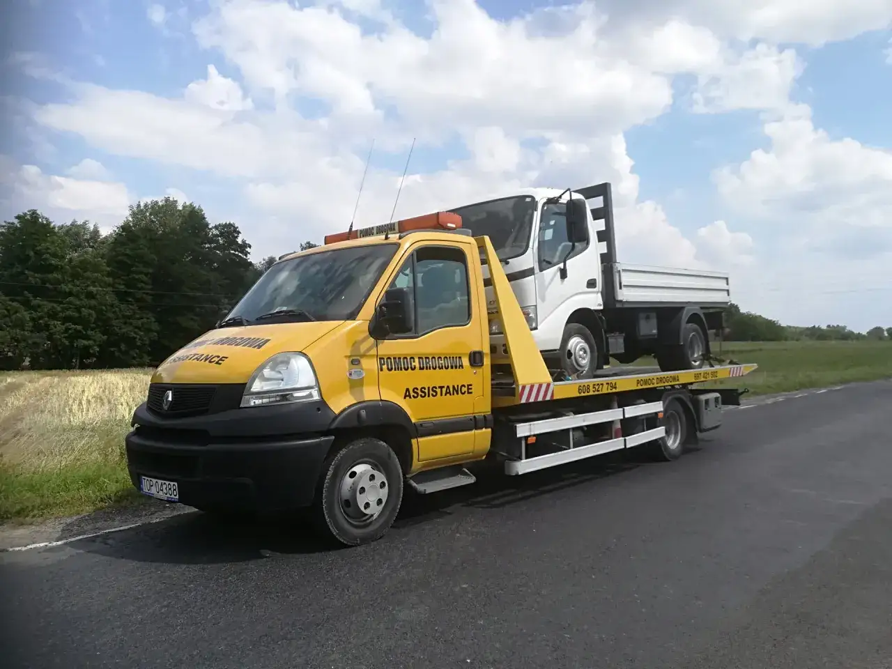 Żółta laweta z białym samochodem na pokładzie. Zastanawiasz się, ile kosztuje laweta? Zadzwoń pod numer 608 527 794.