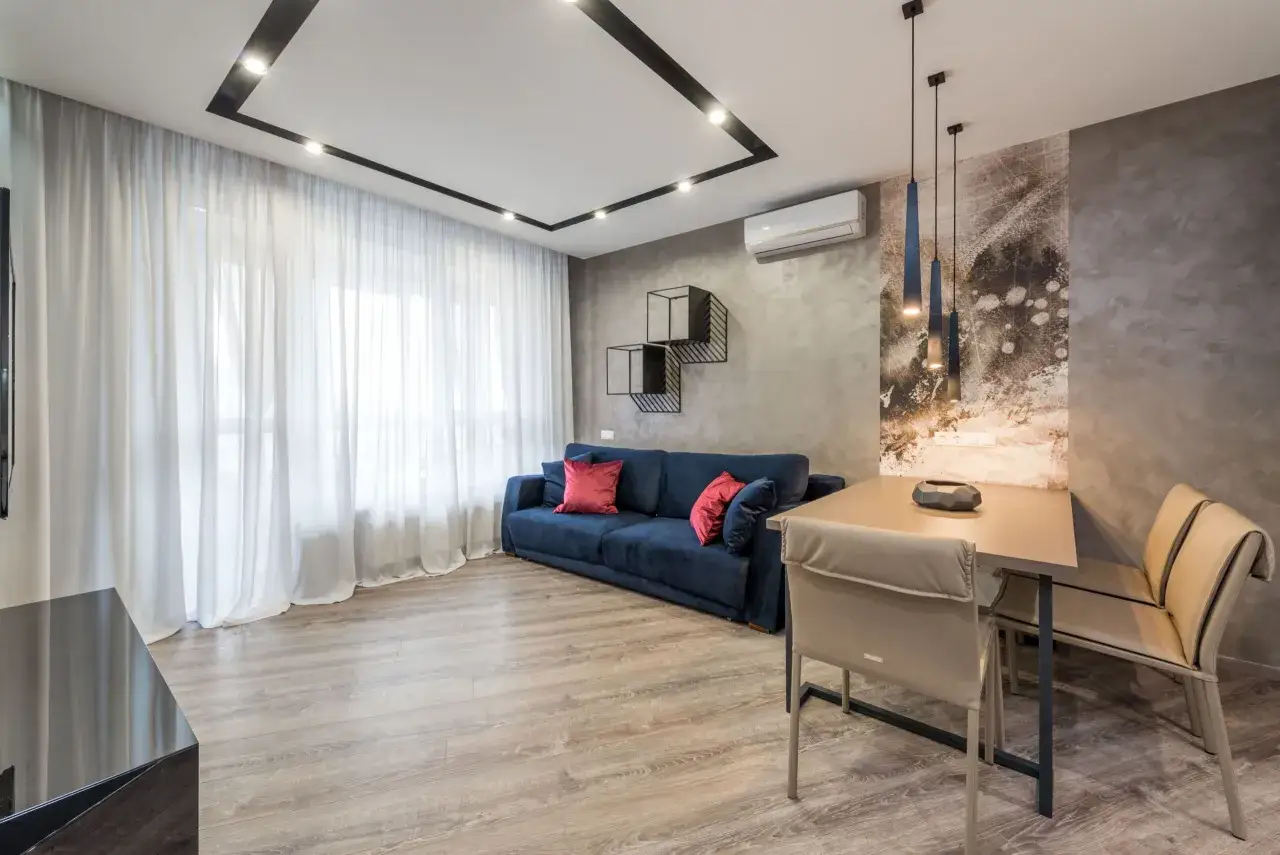 Nowoczesny salon z granatową kanapą, stołem i krzesłami. W centralnym punkcie znajduje się elegancki sufit podwieszany z wbudowanym oświetleniem.
