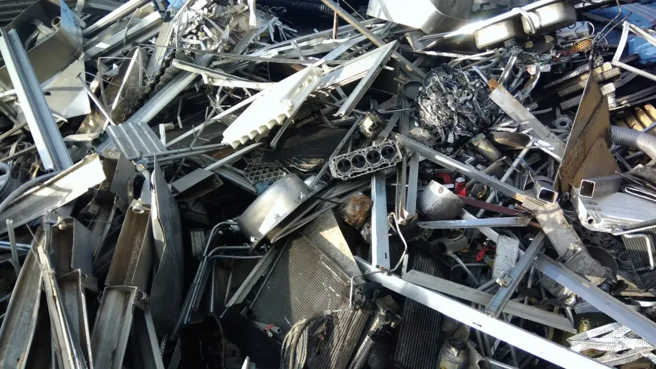 Góra złomu z elementami aluminiowymi, w tym chłodnicami i częściami silnika. Widać potencjalną cenę aluminium na złomie.