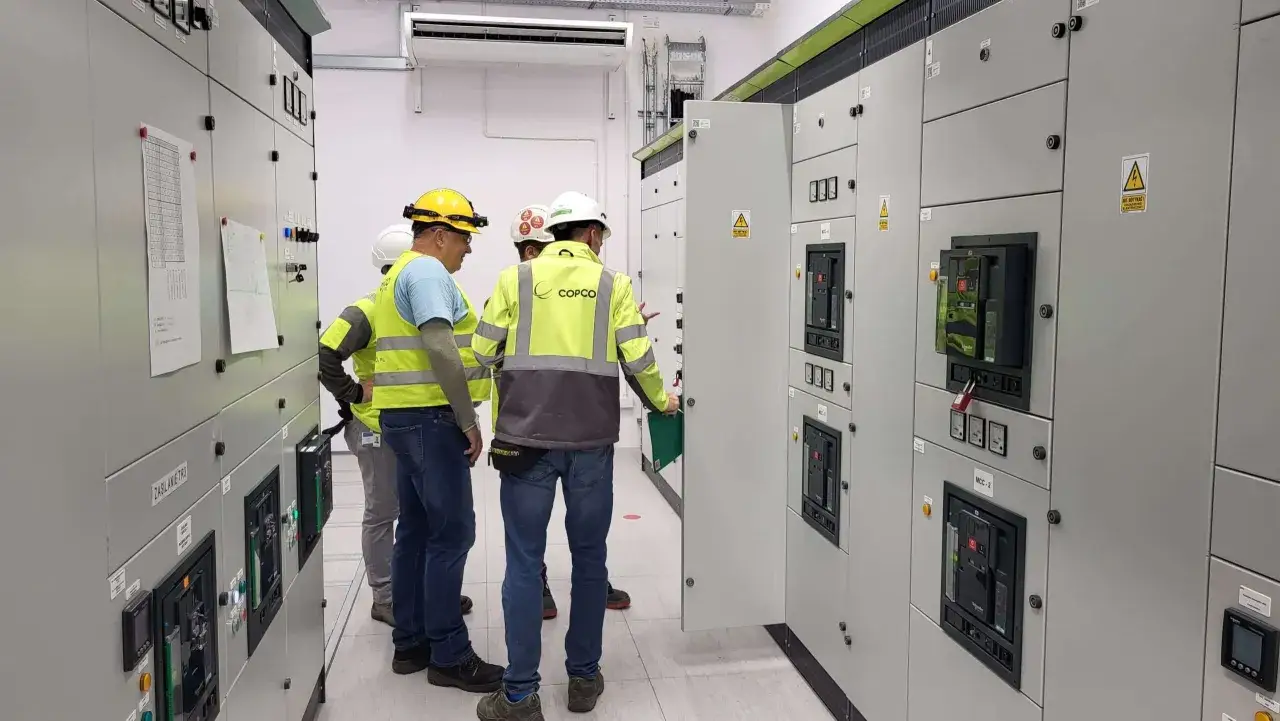Elektrycy w żółtych kamizelkach i kaskach przy panelach sterowniczych. Zastanawiasz się, ile zarabia elektryk?