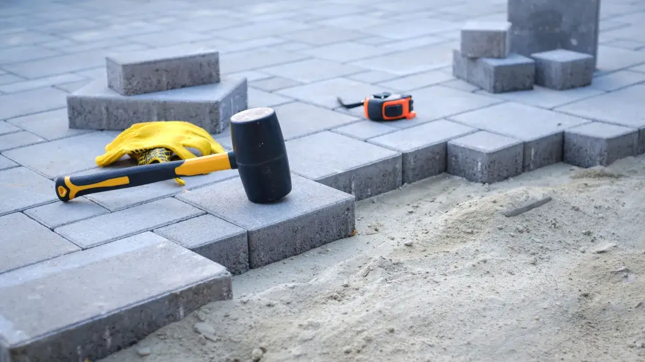 Układanie kostki brukowej. Młotek gumowy, rękawice i miarka leżą obok. Suchy beton cena 1m3 - materiał na podjazd.