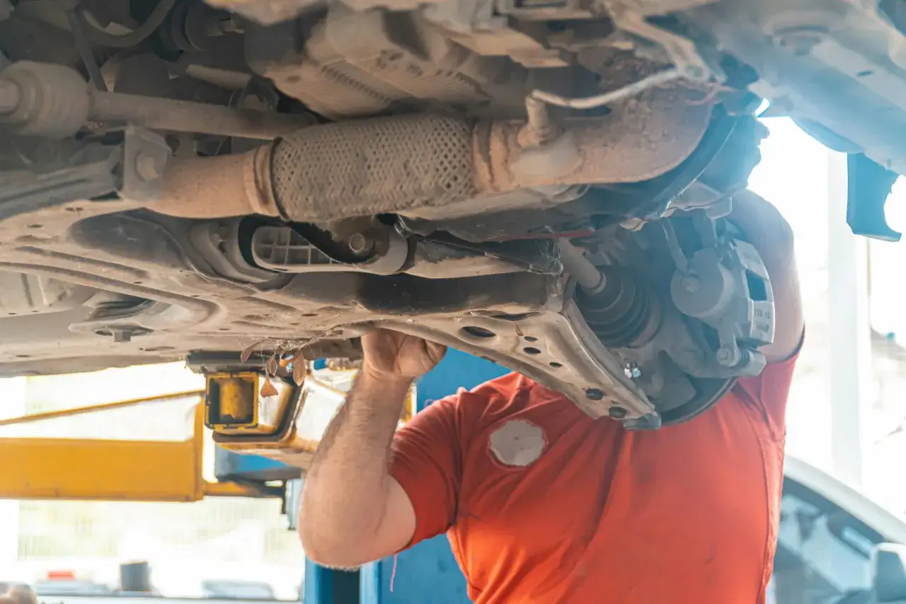 Mechanik pracuje pod samochodem, sprawdzając elementy układu napędowego. Zastanawiasz się nad wymiana sprzęgła koszt?
