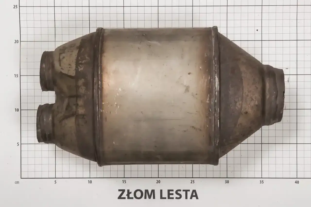 Używany katalizator samochodowy na tle siatki pomiarowej. Sprawdź aktualną cenę katalizatora na złomie.