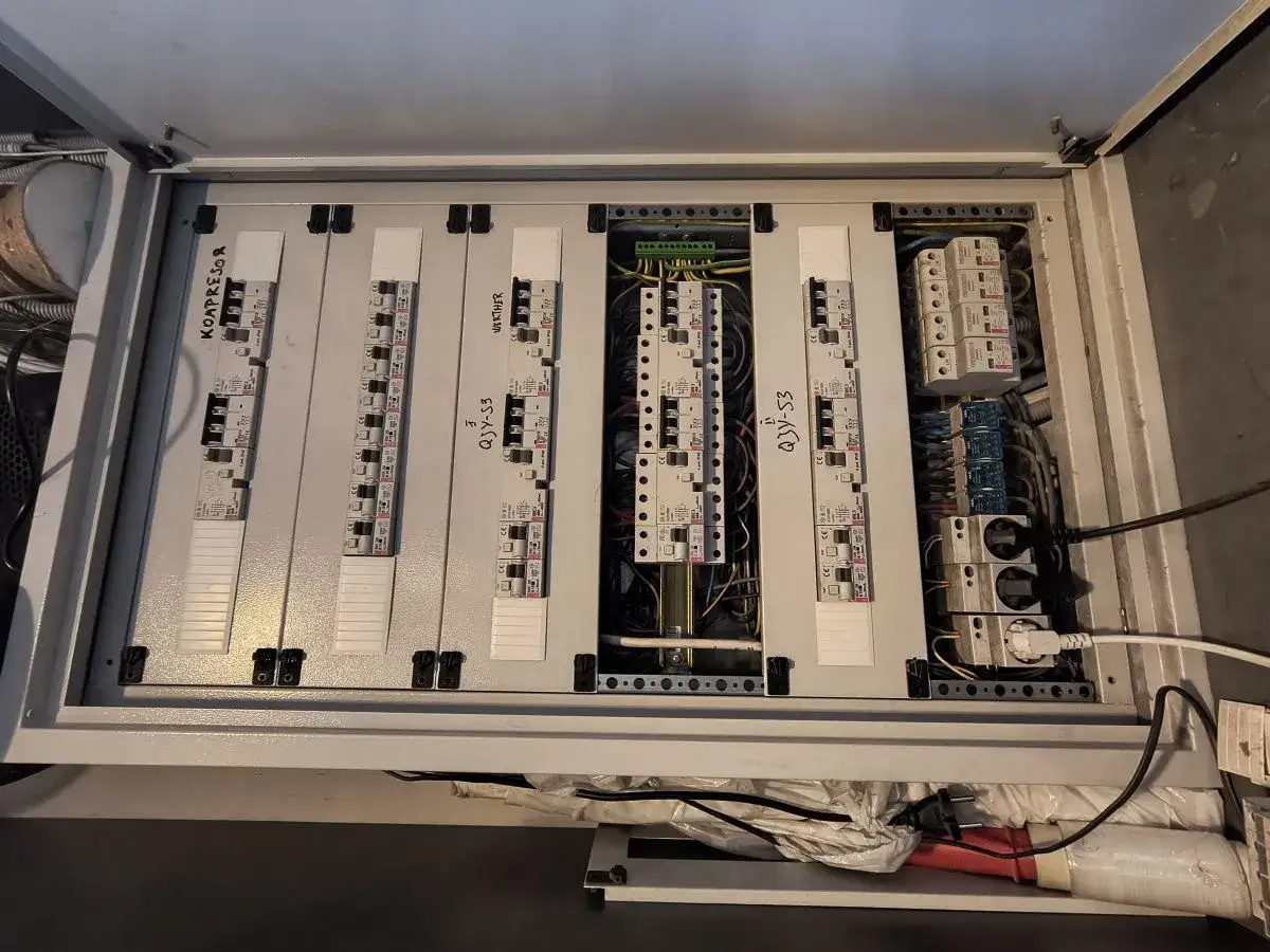 Wnętrze rozdzielnicy elektrycznej z zabezpieczeniem przedlicznikowym. Widoczne wyłączniki, bezpieczniki i okablowanie.