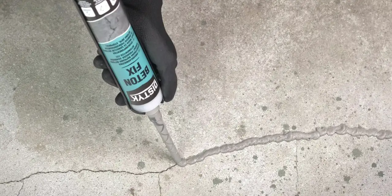 Rękawiczka i pistolet z masą Distyk Beton Fix uzupełniają ubytki w betonie na zewnątrz, naprawiając pęknięcia.