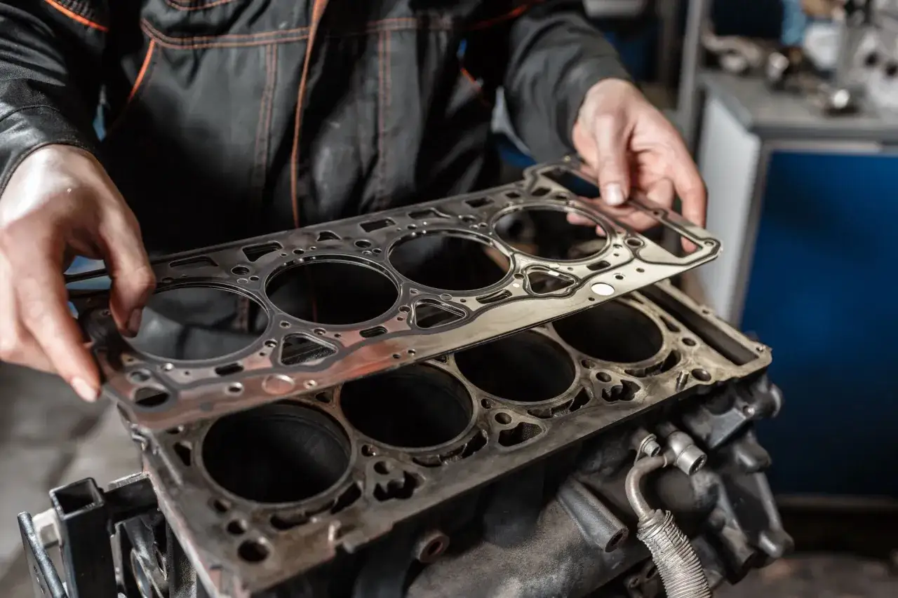 Mechanik trzyma nową uszczelkę pod głowicę nad blokiem silnika, przygotowując się do jej wymiany.